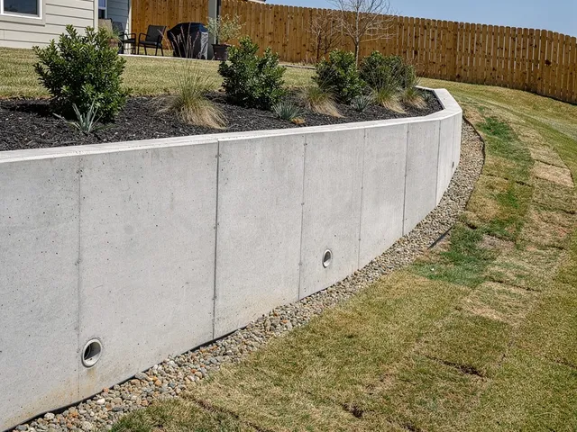 Concrete retaining wall holding back a sloped yard in Pearland, Texas with drainage